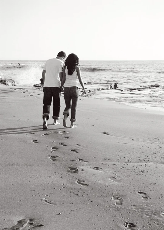 two people walking down a beach, carrying a surfboard