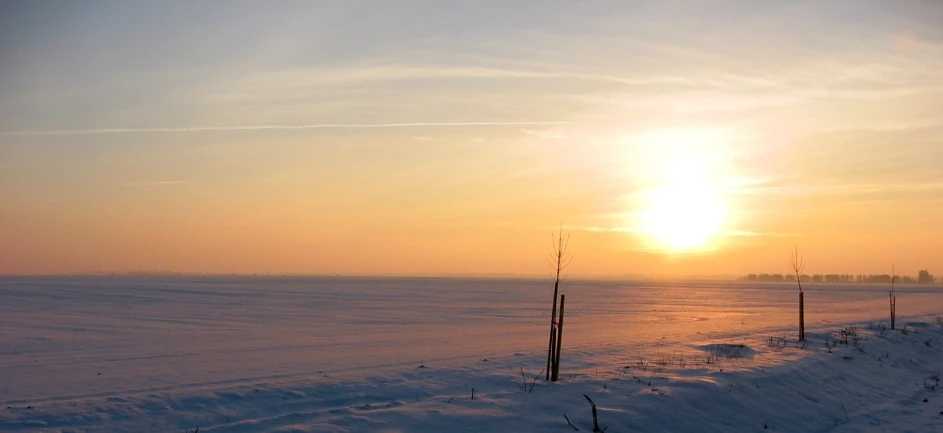 a sunset over an open snow covered field