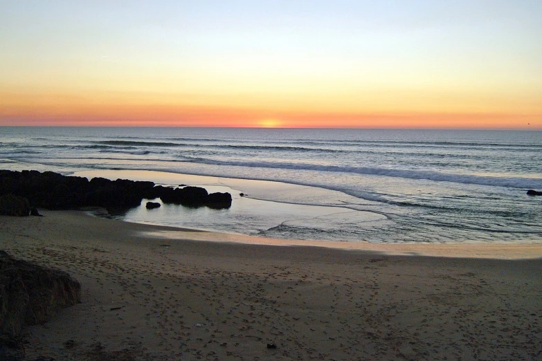 the sun sets over the ocean and a beach