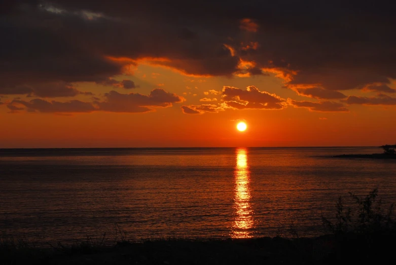 the sun sets over the water as a boat approaches