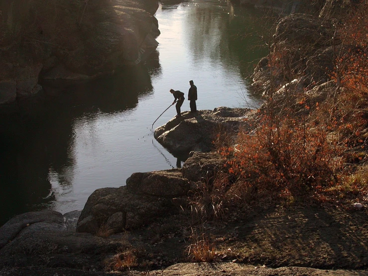 a couple of people standing on top of a cliff by a river