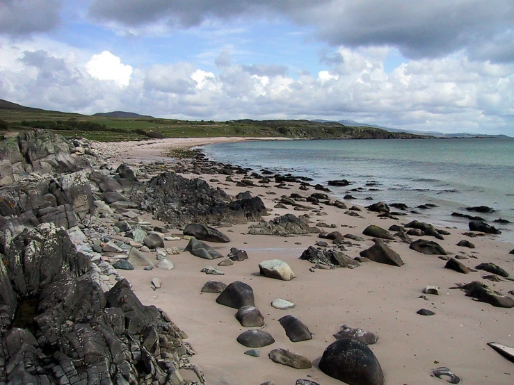 a sandy beach with rocks and water underneath clouds