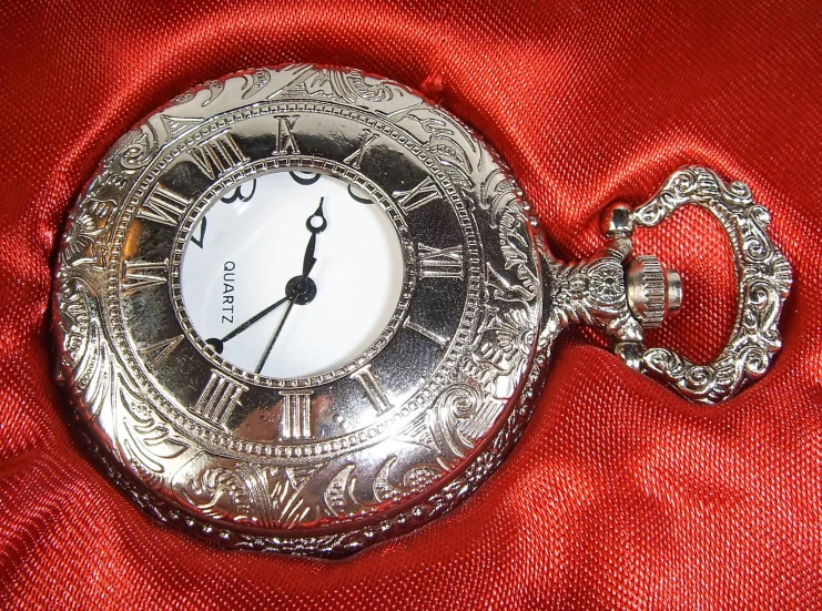 silver pocket watch sitting on a red surface