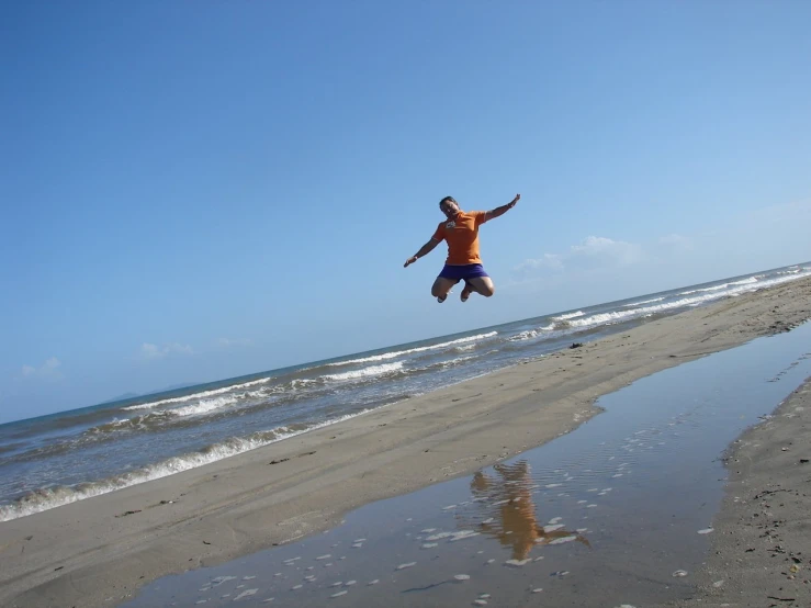 the boy is jumping to the beach with his frisbee