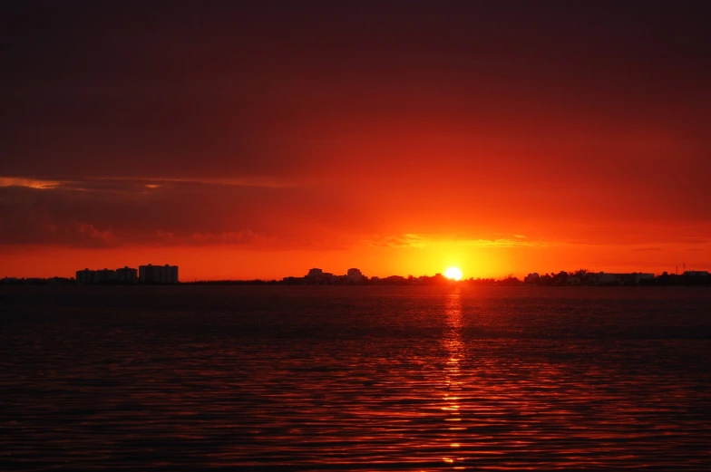 a sun setting over water with buildings in the background