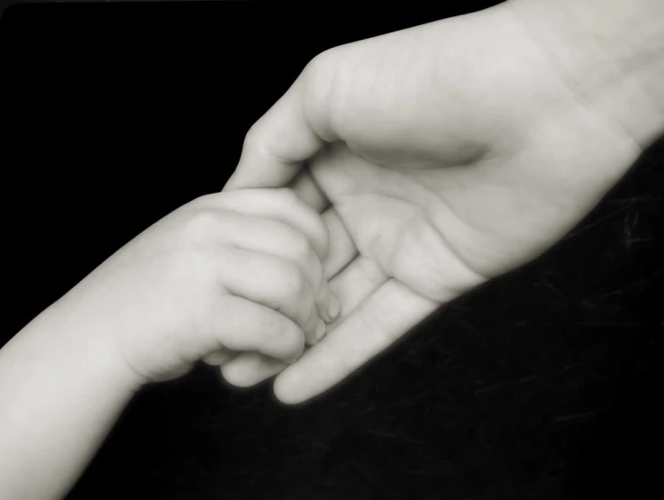 black and white pograph of a child's hand holding the wrist of his parent