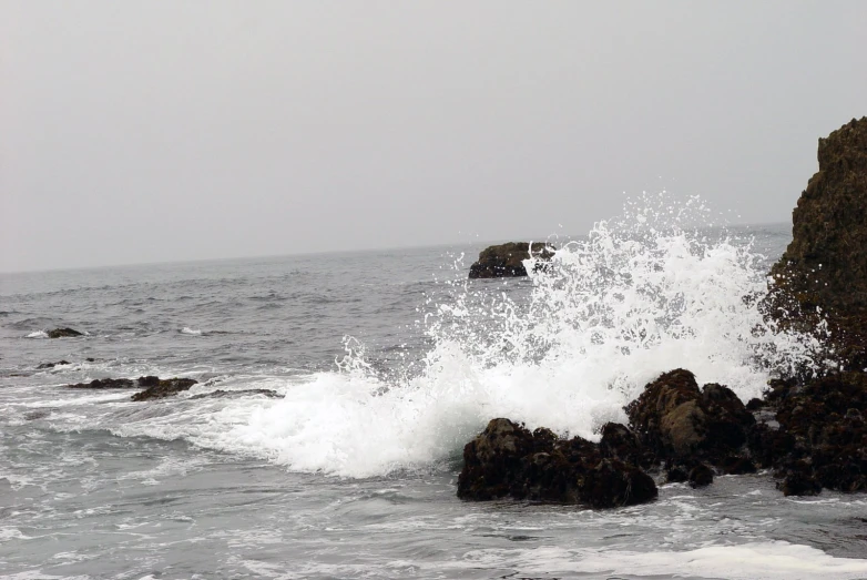 a wave splashing on rocks next to the ocean