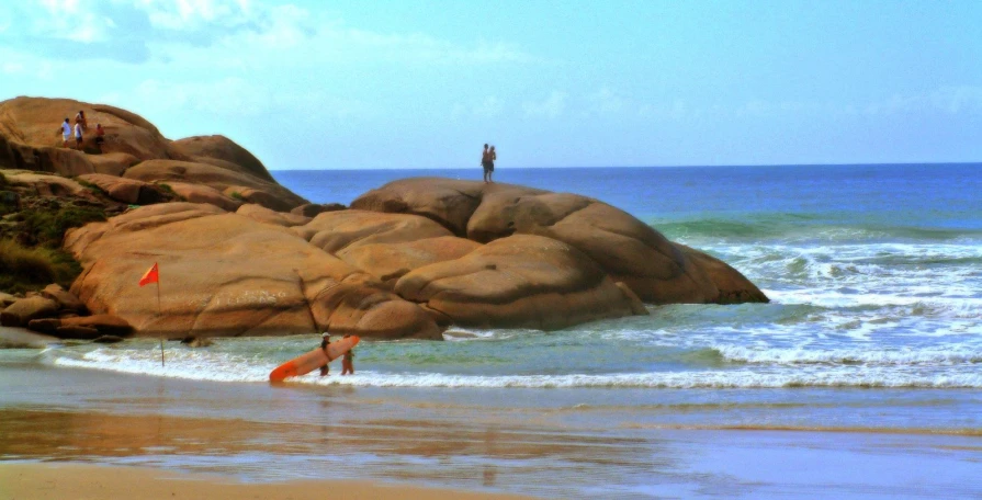 two surfers are walking in the waves next to large rocks