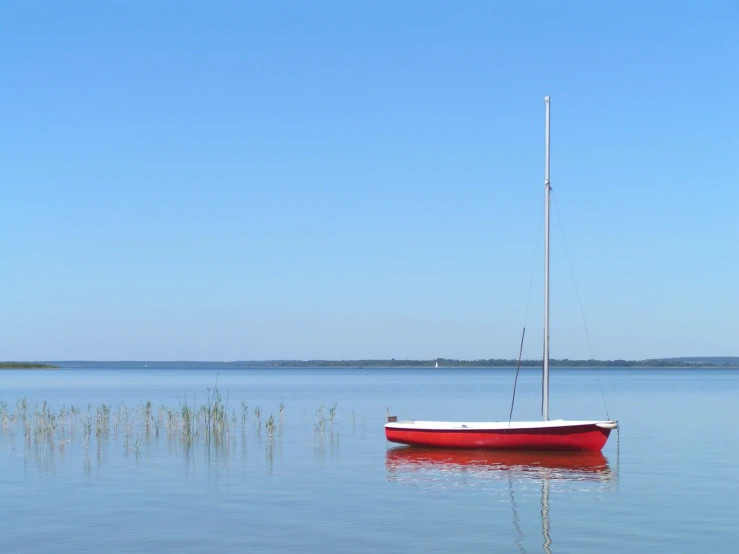 a small red sail boat sits at anchor in shallow water