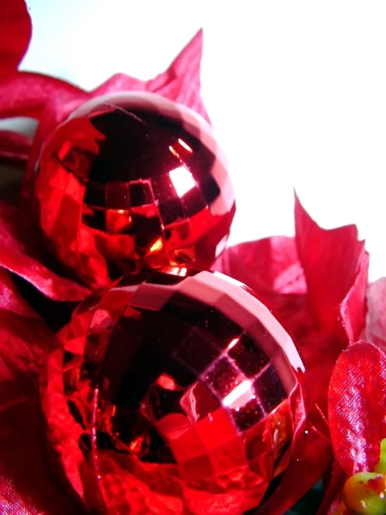 shiny red ornaments sit in a pile on top of flowers