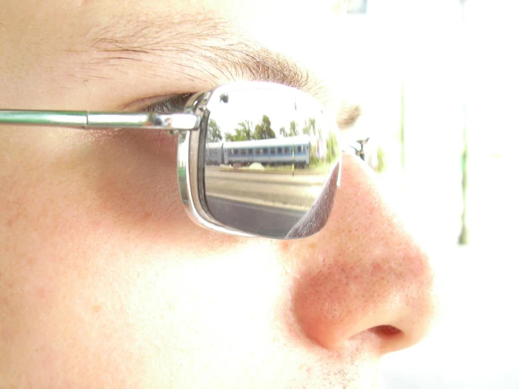 a man wearing silver sunglasses with a train reflected in the lens