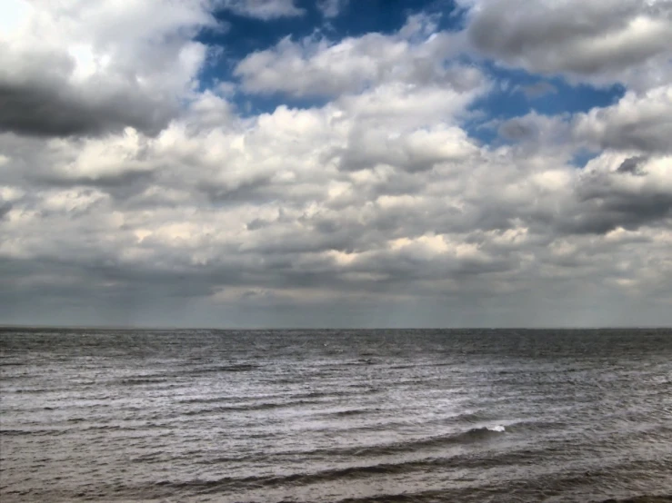 the cloudy sky is over the ocean, and some birds are flying in the sky