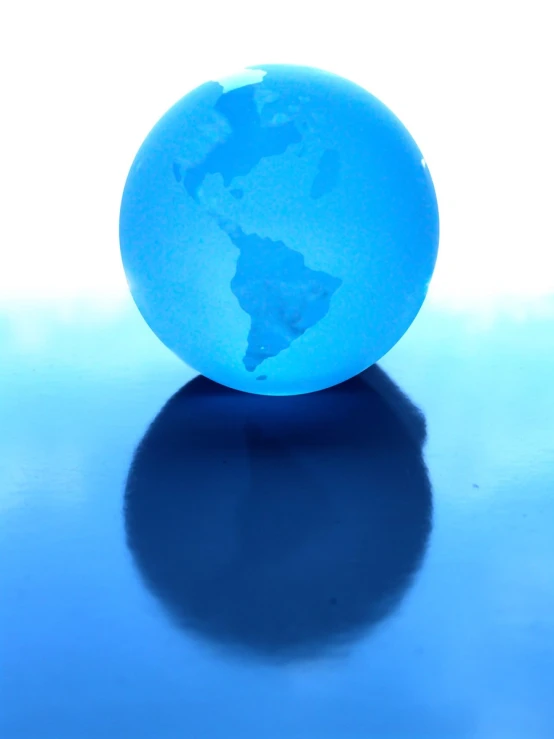 a small globe of the earth sitting on a reflective surface