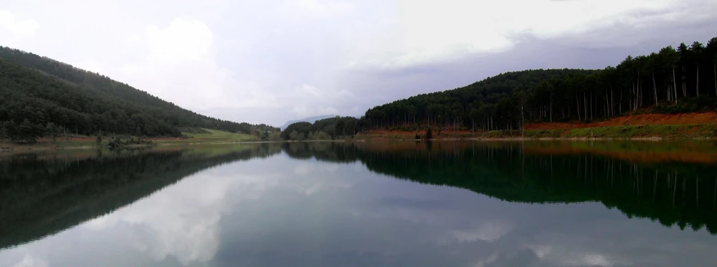 a lake surrounded by green trees under cloudy skies