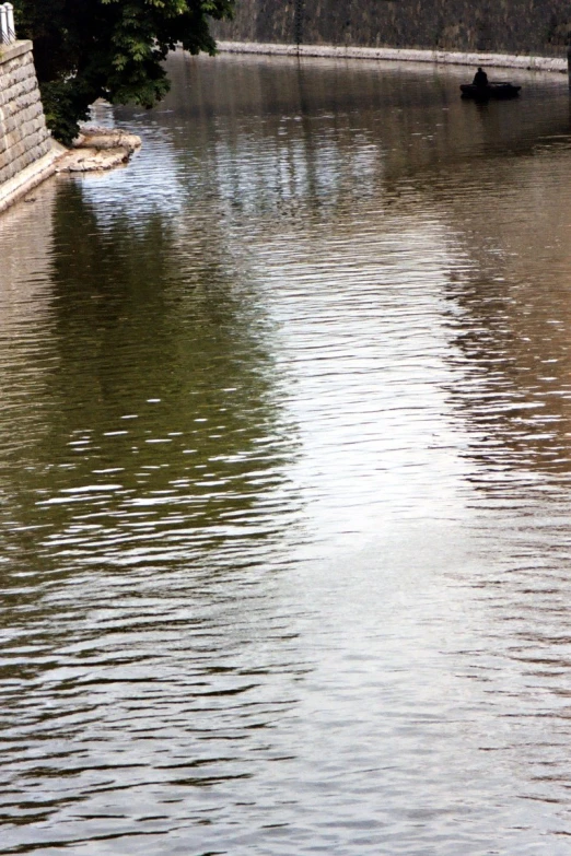 a man fishing in a lake by a stone wall