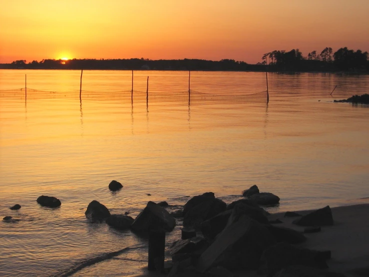 sunset over the water with rocks and poles in the foreground