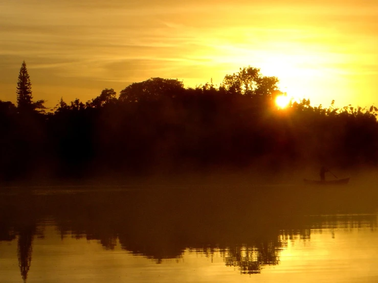 a lake with a person rowing a boat on it and the sun shining in the sky