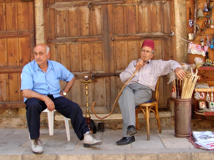 two men sit outside talking while holding a cane