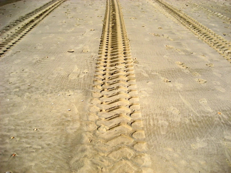 tire tracks in the sand with a truck driving behind them