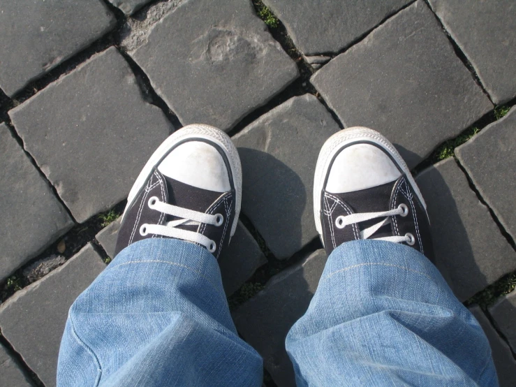 someone's legs in sneakers as they sit on a stone sidewalk