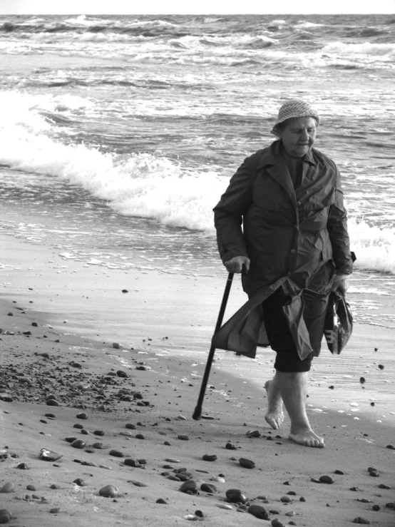 the older lady is standing on the beach with her cane