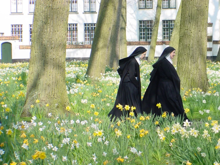 two nun women in long black dresses are walking through the flowers in front of a white building