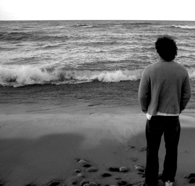 a man stands alone on a beach watching the ocean