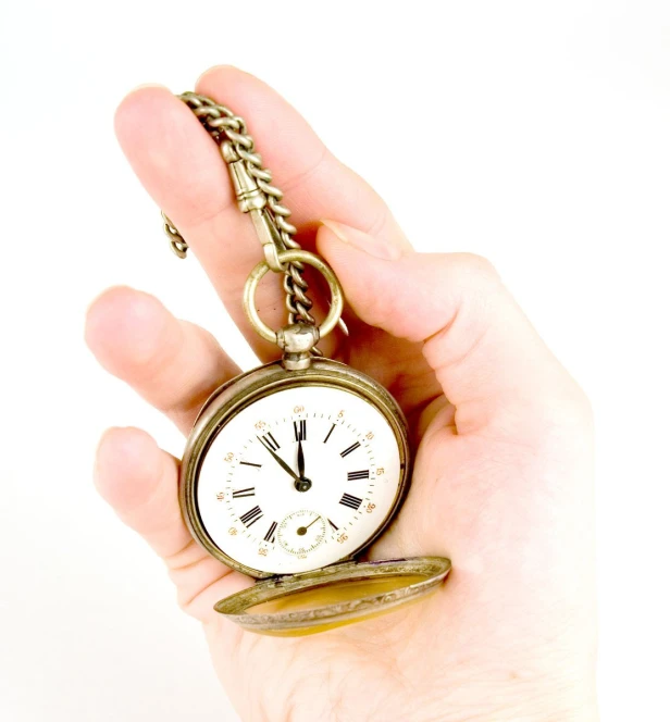 a gold tone pocket watch is being held by a hand