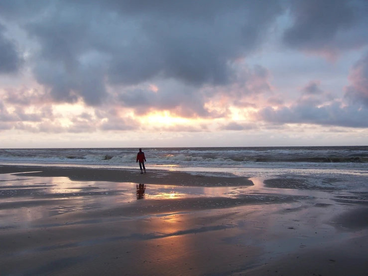 person standing on beach looking out at the ocean at dusk