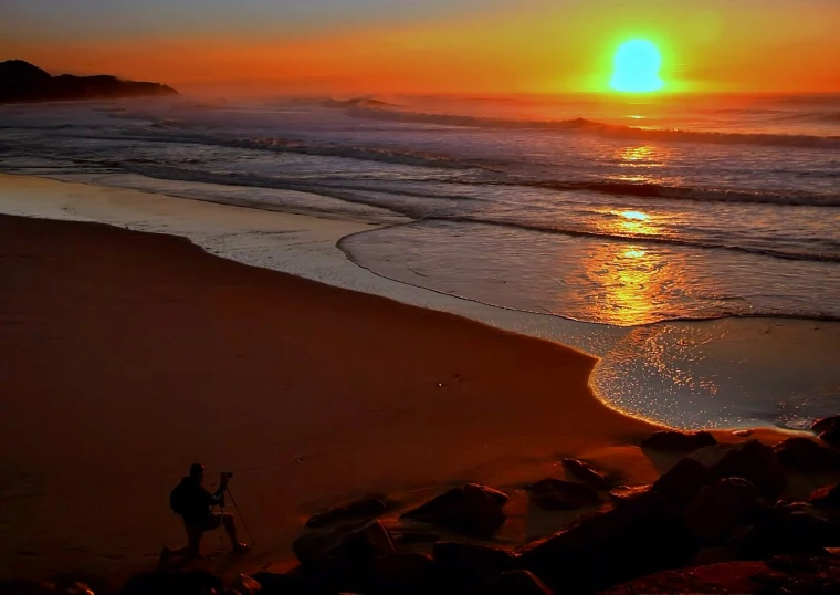 there is a surfer standing on the beach watching the sun rise