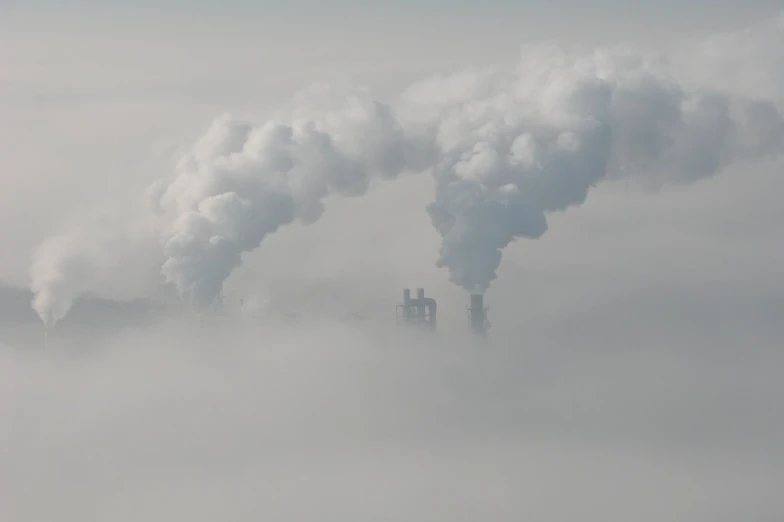 smoke stacks from industrial smokestacks rise above clouds in the sky