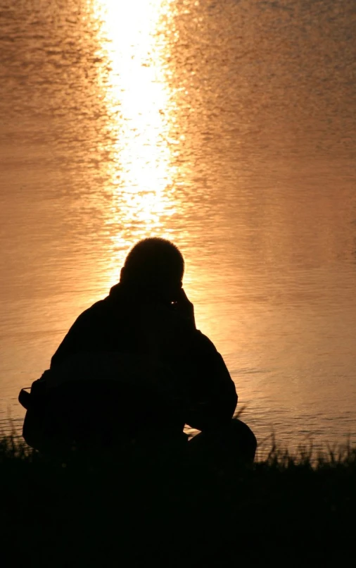 a person is sitting in the shadow near a body of water