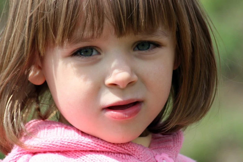 a little girl with brown hair wearing a pink shirt