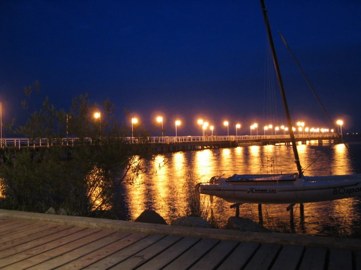 a sailboat sitting on the river next to a dock at night