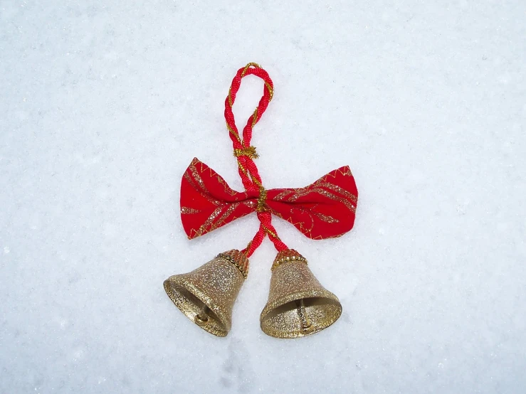 two bells are hanging in the snow in a festive bow