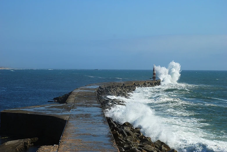 an ocean wave is crashing onto the breakwall of the pier