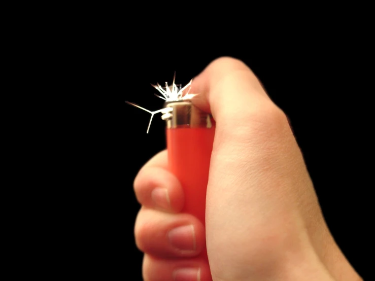 a person holding a small red lighter and sticking it into their finger