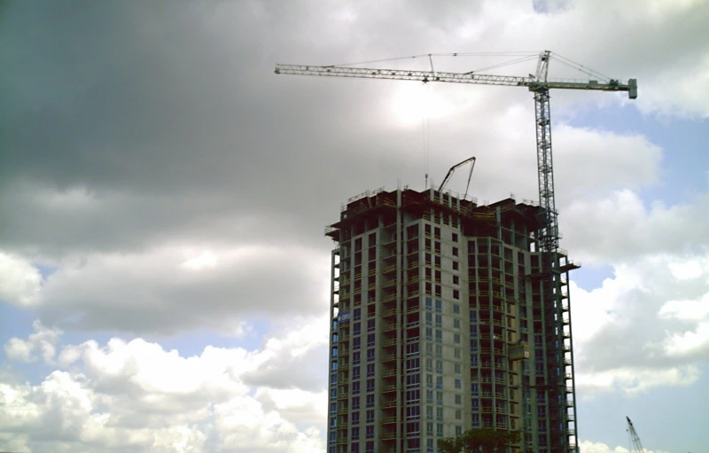 construction cranes against cloudy sky in front of a large building