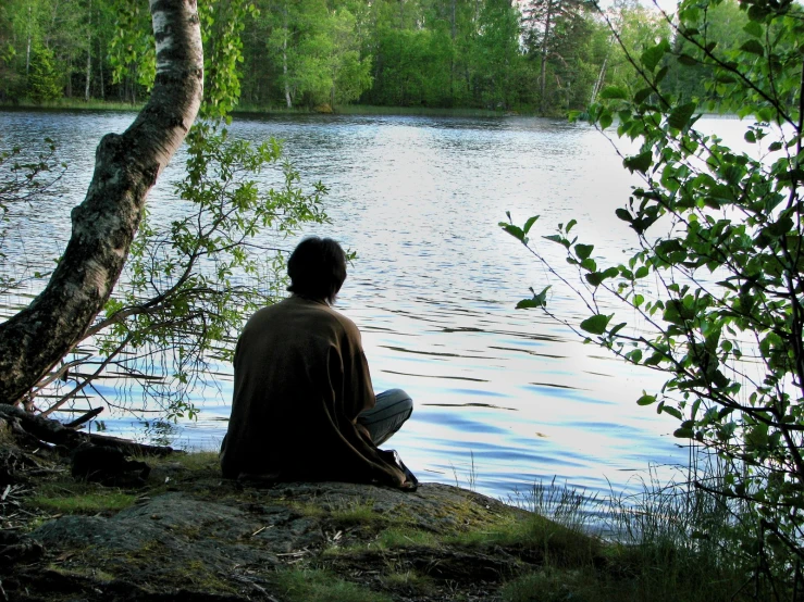 a man sitting next to a lake while looking at the water