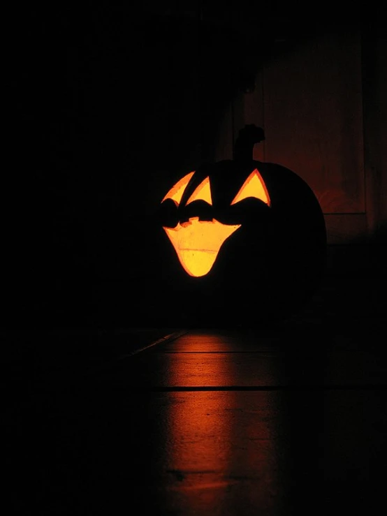 a lighted pumpkin that has its reflection on the ground