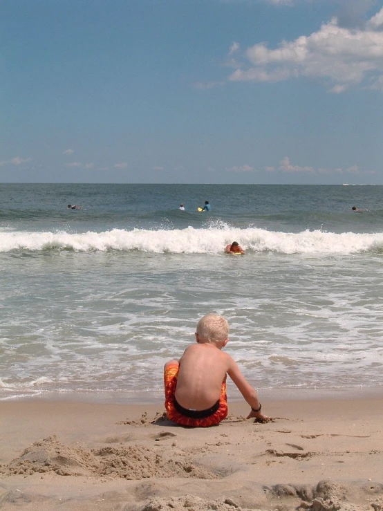 an older man sits on the beach watching a small wave