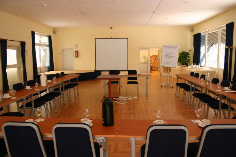 a classroom area with several tables, black chairs and a large projection screen