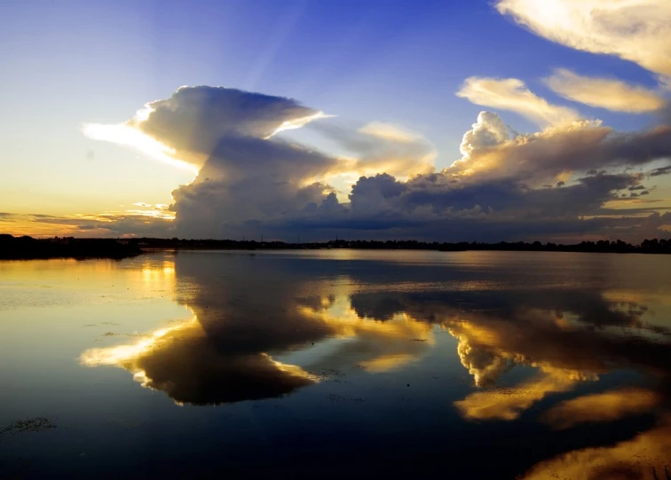 a cloud hangs over a calm lake as the sun goes down