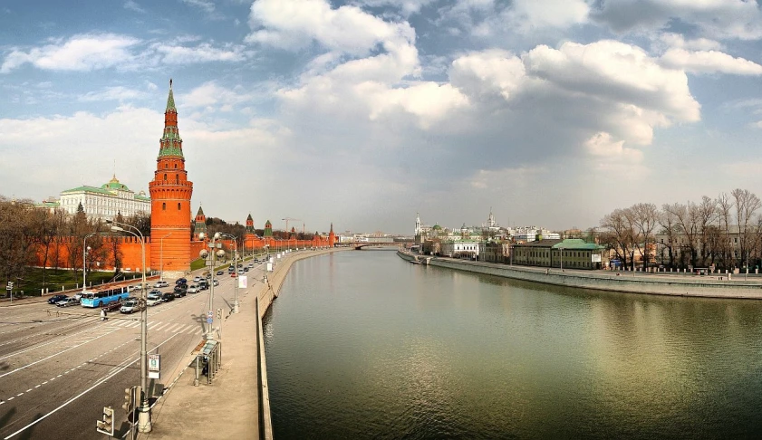 a city street next to the river with some vehicles driving down the road