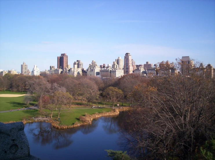 there is a large lake in the park with the city behind it