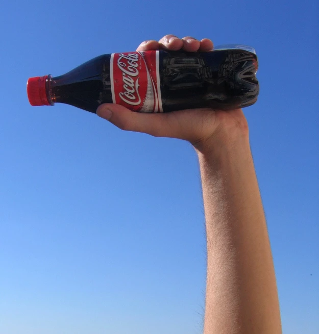 a bottle of coca cola being held up in the air by a hand