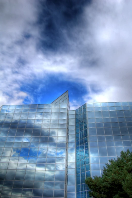 clouds and trees are reflected in windows on the facade of a building