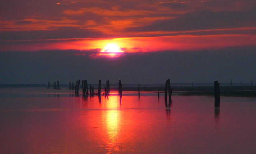 a sunset view over a body of water with long wooden posts sticking out of the water