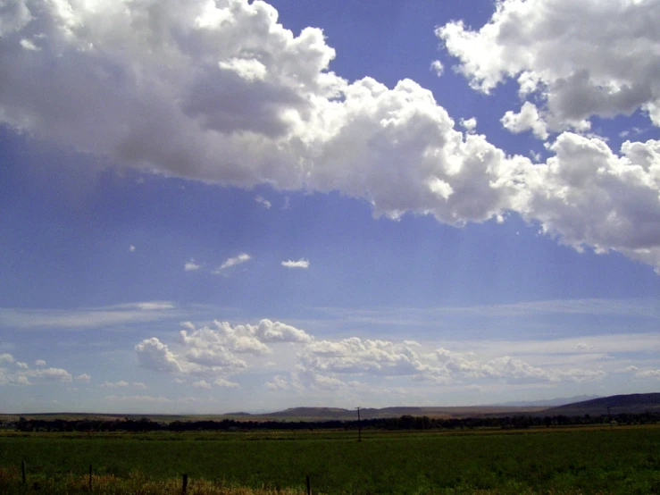 a large grassy field with clouds above it