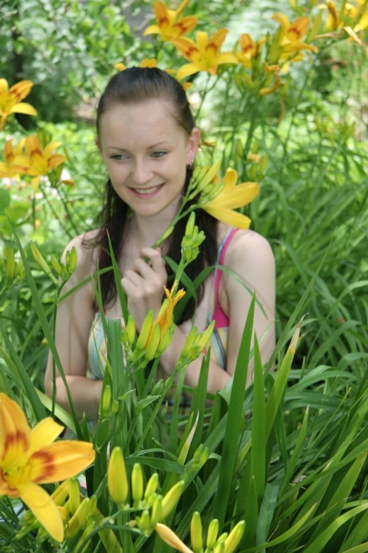 the young woman smiles at the camera from behind some yellow flowers